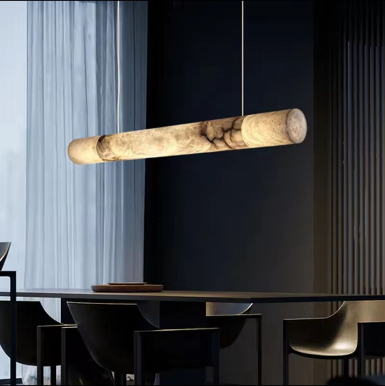 Modern pendant light hanging above a dining table with a dark wall and light curtain in the background.