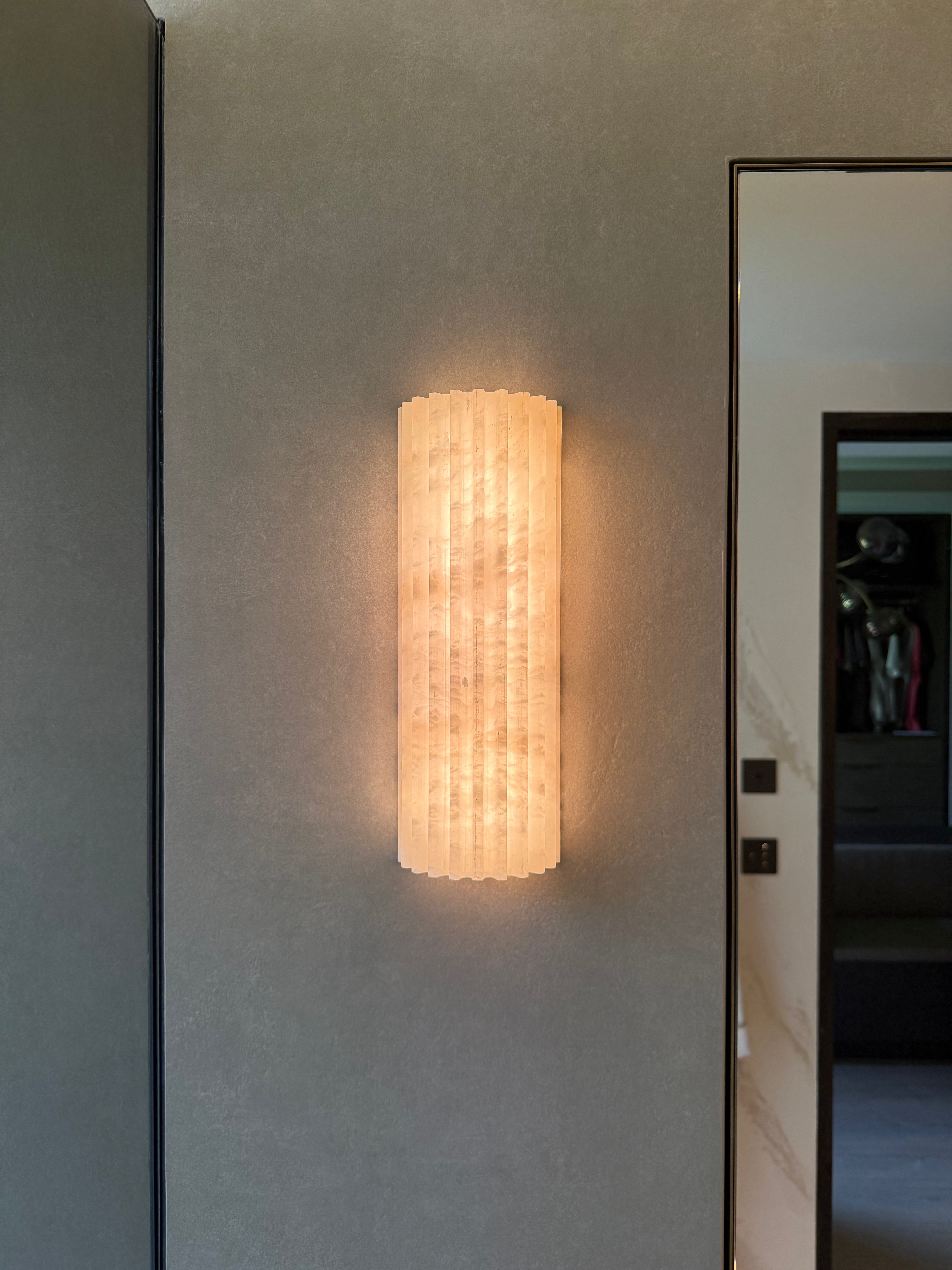 Wall-mounted light fixture on a gray wall with a mirror reflection.